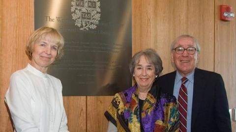 Two women and a man standing in front of a plaque commemorating a new building.