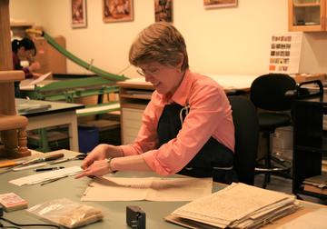 A woman at a bench working with paper objects.
