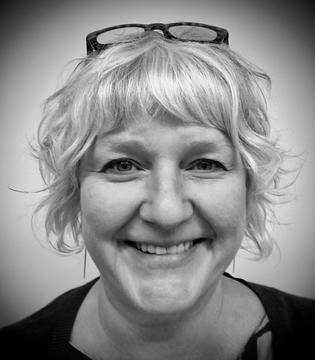 a black and white photo of a woman with short wavy white hair and glasses on top of her head.
