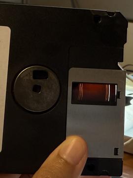 Photograph of a floppy disk with scrapes on the inner media, visible with backlighting, it appears as rings where the heads scraped the binder off as it spun in the drive.