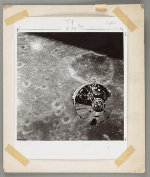 A black and white photograph of the moon with a satelite in the foreground.