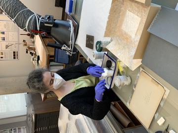 A person cleaning a photograph with a small fume hood trunk above. 