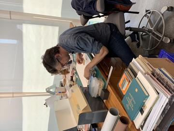 A person working on a small parchment object at his bench. 