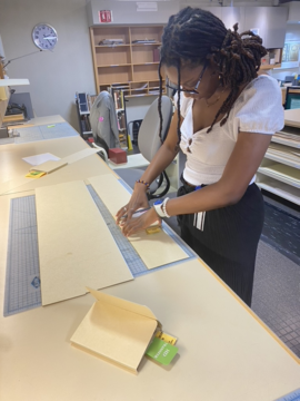A woman measuring cardstock for a box. 