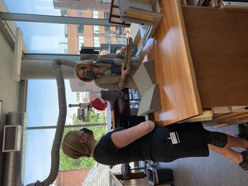 Two people standing at a work bench discussing a book. 