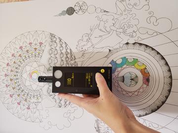 A hand holds an Elsec light monitor in front of a colorful image to measure light levels in a new display case.