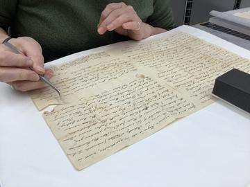Hands doing paper repair on a fragile object. 