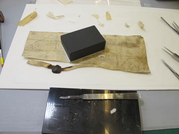 A parchment document during repair with tools and materials around.