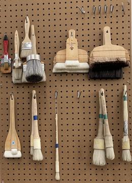 A peg board full of brushes of various sizes with wooden handles.