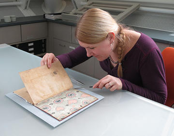 A woman carefully examining a manuscript with a small spatula.