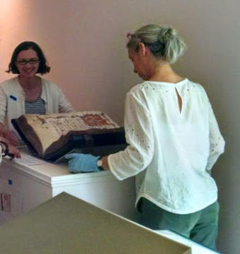 Two people stand on either side of a display case with a large book open between them.  