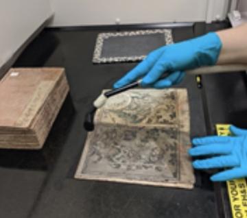 A gloved-hand vacuuming mold from a book page.