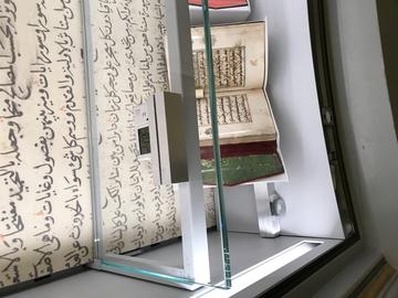Two monitors which record light levels, temperature and relative humidity are shown in a display case alongside displayed books.