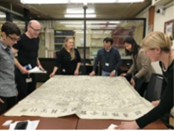 A group of people around a table with a large folded map opened up covering the whole table.