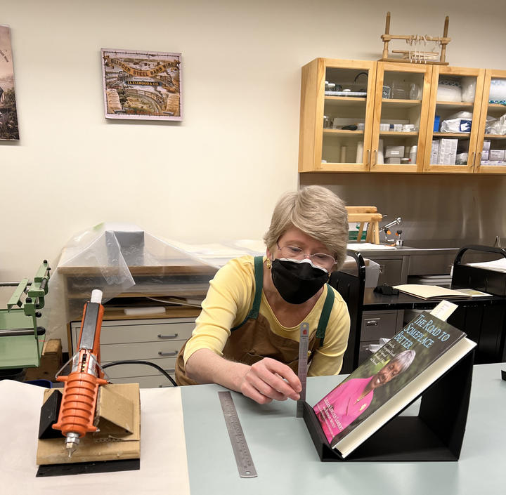 A woman making a cradle out of mat board for a book.
