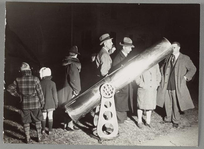 A photograph depicting a group of people outside at night with a small telescope.  