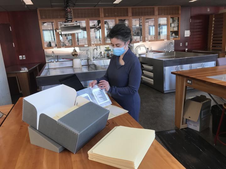 A woman wearing a mask looking through folders of photographs.