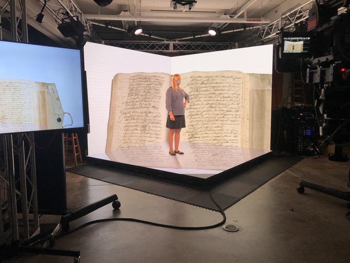 A woman standing in front on and in front of screens showing the inside of a digitally scanned book.