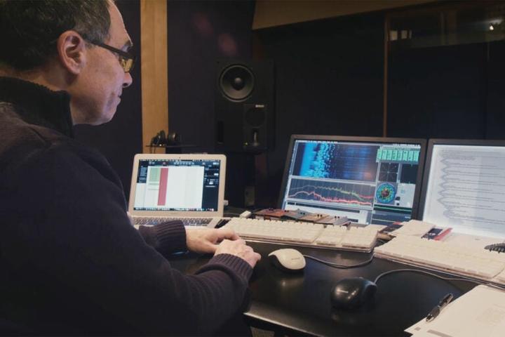 A man sitting in front of multiple monitors with audio digitization software programs running.