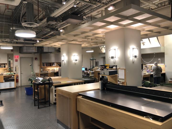 A large open space with workbenches and built-in drawers around the perimeter and cabinets above. Several people are working.
