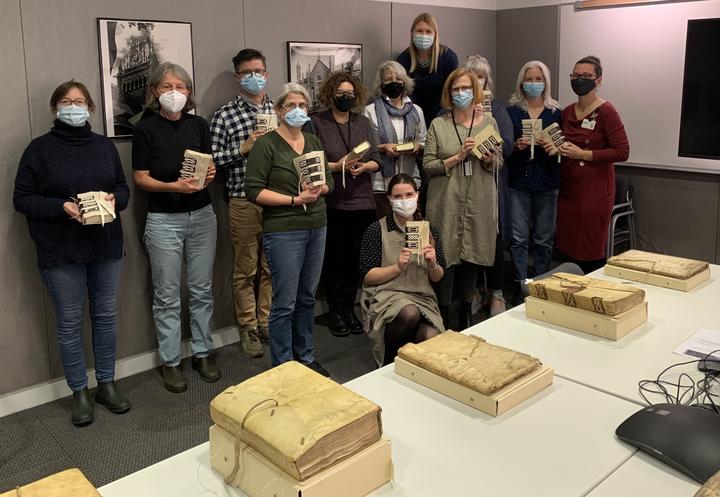 A group of people all holding the models they made in front of a table of the original books.