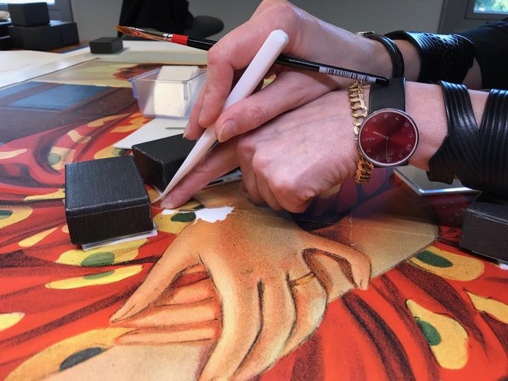 A close up of a pair of hands repairing on a large, colorful poster. 