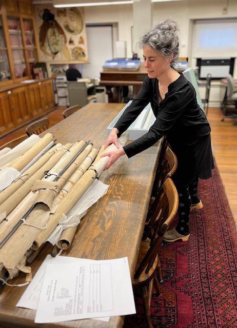 A person grabbing one rolled chart from a pile of rolled charts off a table. 