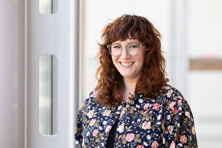 A woman with curly hair and glasses wearing a flower shirt.